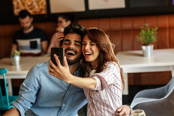 Young couple sitting at the cafe and relaxing on coffee break.They kissing and making selfie.
