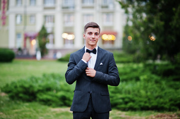 Portrait of a handsome young guy dressed in cool suit posing on the lawn on his prom day. - obrazy, fototapety, plakaty
