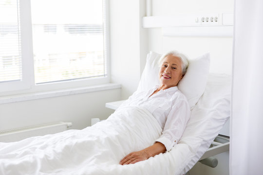 smiling senior woman lying on bed at hospital ward