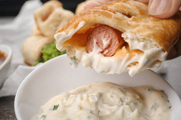 Woman eating tasty sausage roll with sauce, closeup