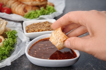 Woman eating tasty sausage roll with sauce, closeup