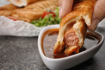Woman eating tasty sausage roll with sauce, closeup