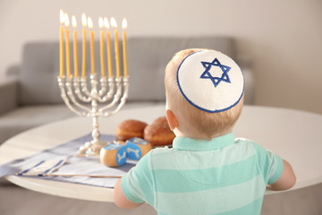 Cute boy sitting near nine-branched menorah on table at home © Africa Studio