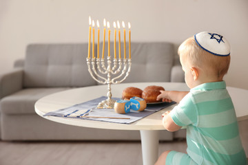 Cute boy sitting near nine-branched menorah on table at home