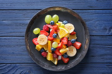 Plate with delicious fruit salad on wooden background