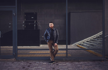Fototapeta na wymiar Bearded man in a leather jacket posing near a glass building