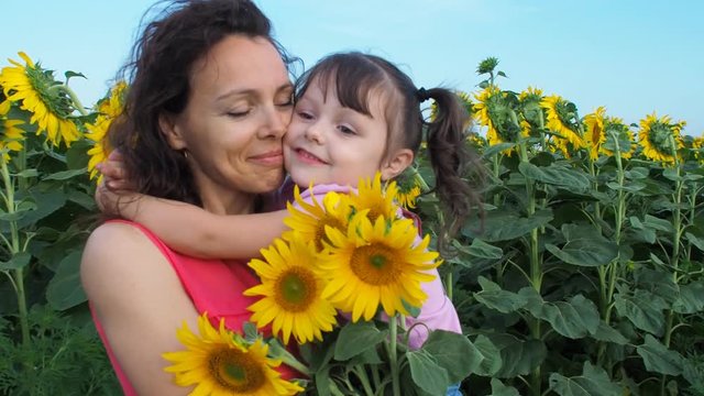 A child is hugging her mother in the field of sunflowers.