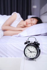 alarm clock on table and woman sleeping on bed in bedroom