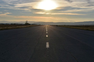 Sunset, flat valley, two people walking on a wide straight empty asphalt road towards the sun at the horizon
