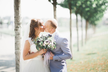 Stylish couple of happy newlyweds walking in the park on their wedding day with bouquet
