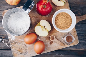 Ingredients for apple pie cooking with fresh red apples, flour, eggs, brown sugar and spices
