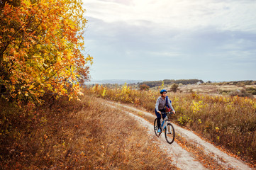 Naklejka premium Young woman riding a bicycle in the autumn field