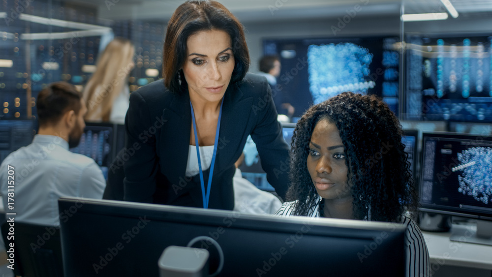 Poster Female Team Leader Consults Young Computer Engineer. They Work in a Crowded Office on a Neural Network/ Artificial Intelligence Project.