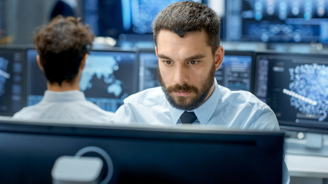 Neural Network and Machine Learning Engineer Programming at His Workstation. Office is Crowded With People Working. Multiple Displays Show Neural Network, Artificial Intelligence Representation.