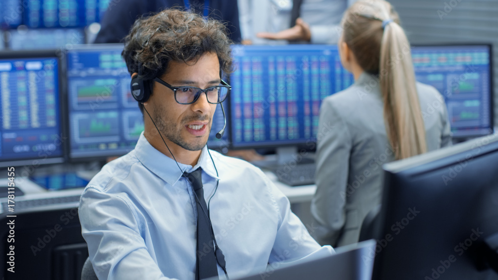 Leinwandbilder Stock Trader Making Sales with a Headset. In the Background Stock Exchange Office and Group of Traders Working at their Workstations.