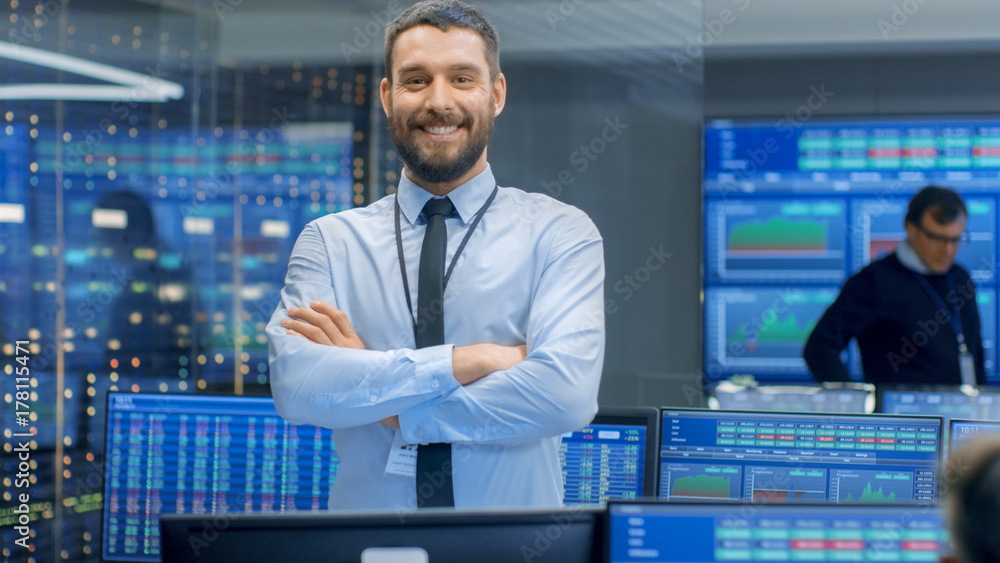 Poster successful male stock trader crosses arms and smiles at the camera. in the background busy stock exc