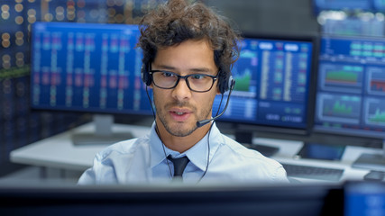 Broker Making Sales with a Headset with His Multi-Ethnic Team of Stock Traders at the Stock Exchange Firm Office is Busy Selling and Buying Bonds and Shares. Displays Show Relevant Graphs and Numbers.