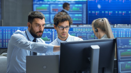 Professional Broker Consults Stock Exchange Trader at His Workstation. Multi-Ethnic Team at Stock...