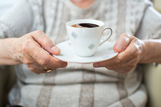 Closeup of wrinkled senior woman's hands holding coffee cup.