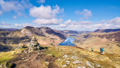 Three hikers descending the summit of Fleetwith Pike, English Lake District with views of High...