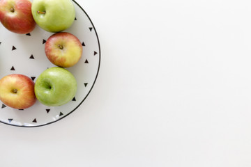 Top view of Red and green apples in white plate with black triangles pattern on upper left corner with white background.