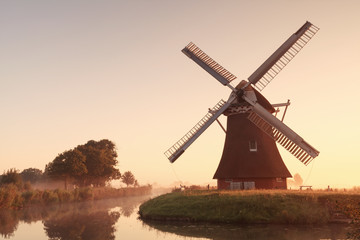 Fototapeta na wymiar charming windmill by river at sunrise