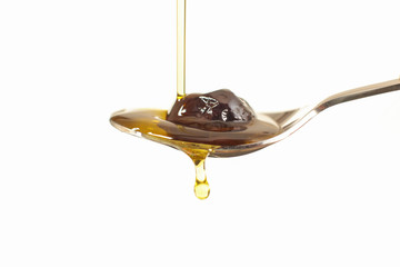 Close up view of virgin olive oil pouring on stainless stell spoon on white background.