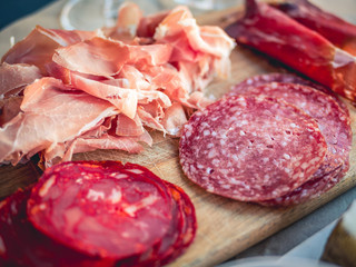 Close up of antipasto platter cold meat plate with prosciutto, sliced ham and salami. On a wood cutting board
