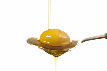 Close up view of virgin olive oil pouring on stainless stell spoon on white background.