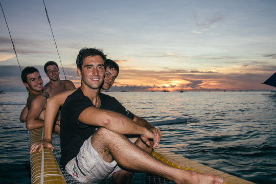 Four male friends on a catamaran boat on the sea at sunset