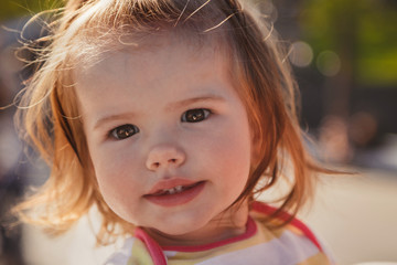 Close up portrait of beautiful small baby, blond little girl in colourful pullover in park outdoors