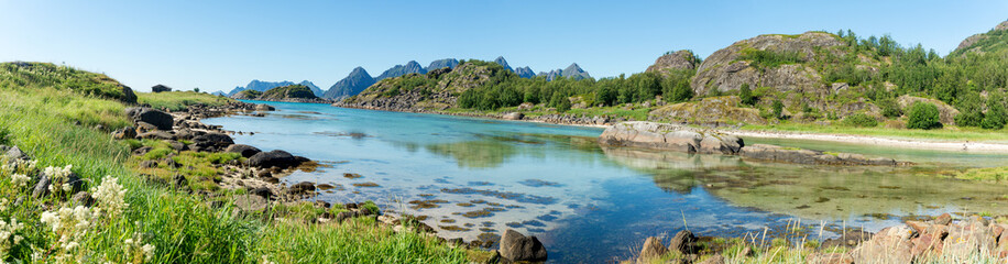 Fototapeta na wymiar The turquoise water of the bay, the stones and the green grass in summer, Arsteinen island, Lofoten, Norway