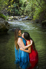 Fototapeta premium Two beautiful women on the bank of a mountain river with evening dresses