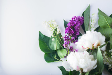 Floral flat lay scene of fresh flowers - lilac, peonies and lilly of the walley flowers on white background