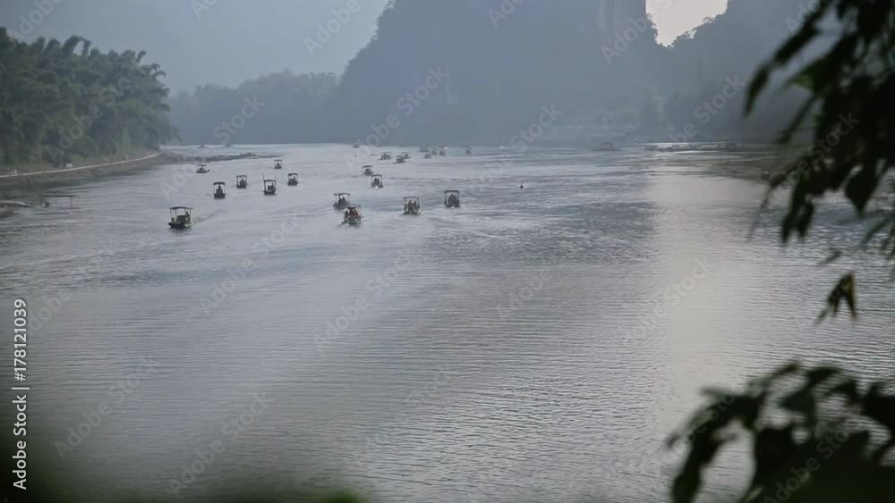 Wall mural Handheld shot of beautiful Yu Long river Karst mountain landscape in Yangshuo. Maby small raft boats floating at sunset. - Wall murals