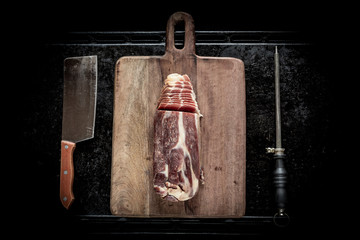 Sliced Jamon on a wooden board, a knife for meat and a grindstone