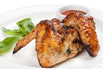 Grilled chicken wings with tomato sauce on a white plate.