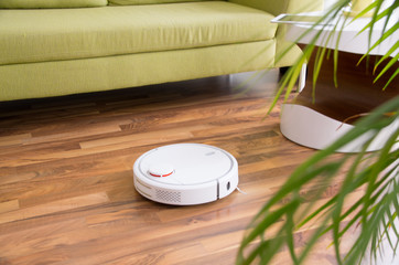 Weißer Staubsaugerroboter / Saugroboter reinigt im Wohnzimmer den Parkettboden / Laminat