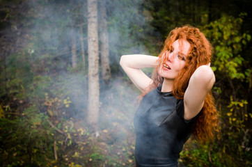 Woman with red curly hair on a forest . Smoke background
