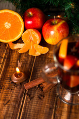 Candle, orange fruit, apple, cinnamon sticks near mulled wine on wooden background. Christmas decoration. New year
