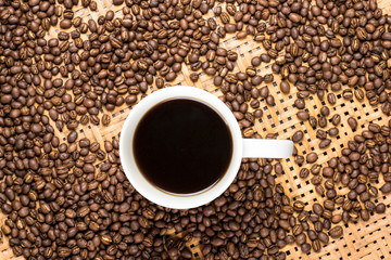 Flay lay style, Medium dark Roasted peaberry coffee beans with black coffee filled in coffee mug on bamboo handcraft background.