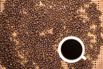 Flay lay style, Medium dark Roasted peaberry coffee beans with black coffee filled in coffee mug on bamboo handcraft background.