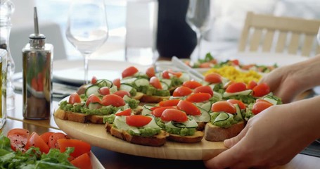 Waiter Serves Beautiful Organic Avocado Sandwiches/ Bruschetta on a Wooden Tray, Table Furnished in Mediterranean Food: Seasonal Vegetables, Olive Oil