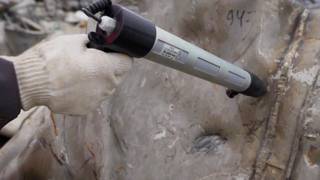 worker of scrap metal processing plant is exploring big piece of metal for detecting radiation outdoor in daytime