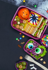 Fototapeta na wymiar Halloween lunch box with school lunch with sandwich and vegetable salad on black background with blank space for text