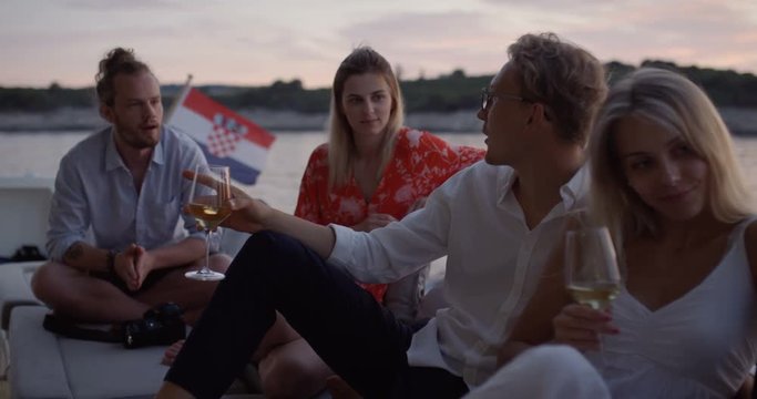 Group of Young People Talk, Drink Champagne in the Stern of the Moving Yacht. They Have Great Vacation. In the Background Island with Small Village. Shot on RED Epic 4K UHD Camera.