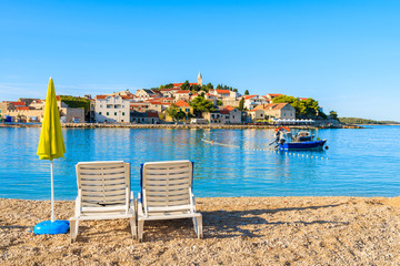 White sunbeds with umbrella on beach in Primosten town, Dalmatia, Croatia