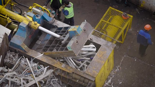 huge hydraulic scrap baling press machine is working, pressed metal garbage in a briquettes in a junkyard in daytime