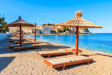 Sunbeds and umbrellas on beach in Primosten town, Dalmatia, Croatia