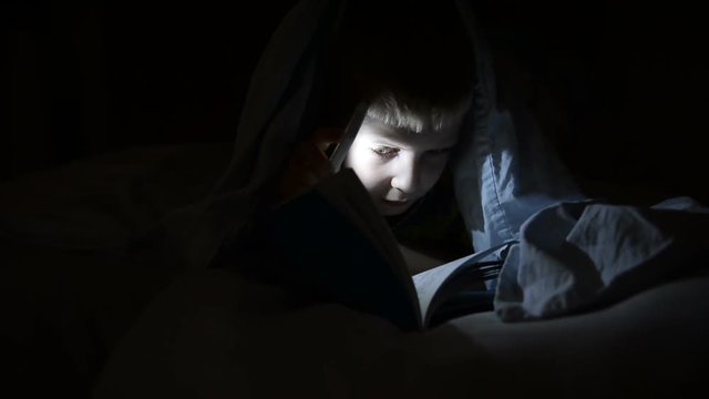 A boy with a flashlight under a blanket is reading a book. Shkolnik, emotions, secrets, horrors, laughter